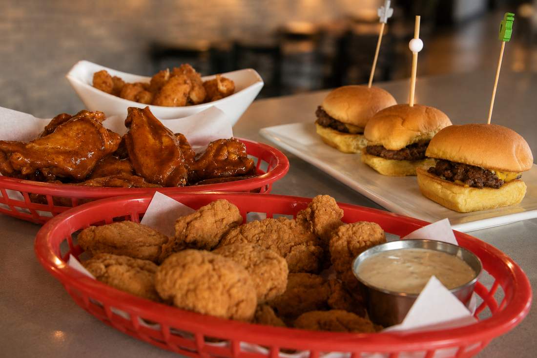 Baskets of saucy wings, cheese curds, breaded chicken, and a plate of sliders on the bar
