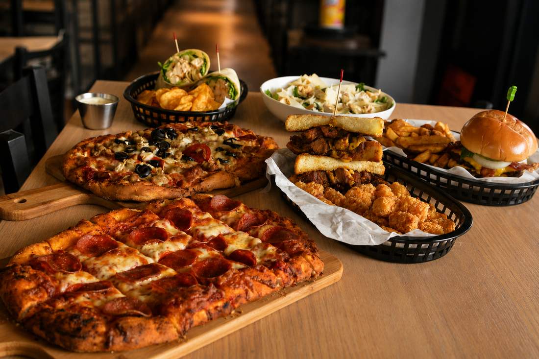 Spread of pizzas, wraps, sandwiches, a burger, and shareables on the table at Putters