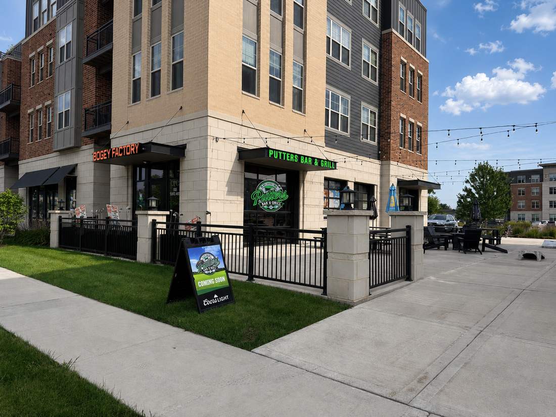 Corner view of Putters Bar & Grill with the glowing green sign and fenced patio