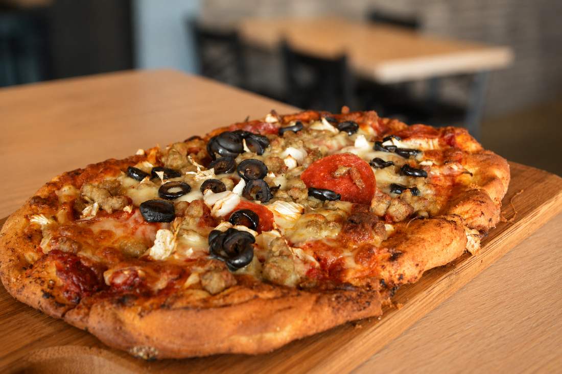 Flatbread pizza with sausage, pepperoni, olives, and onions on a wood board