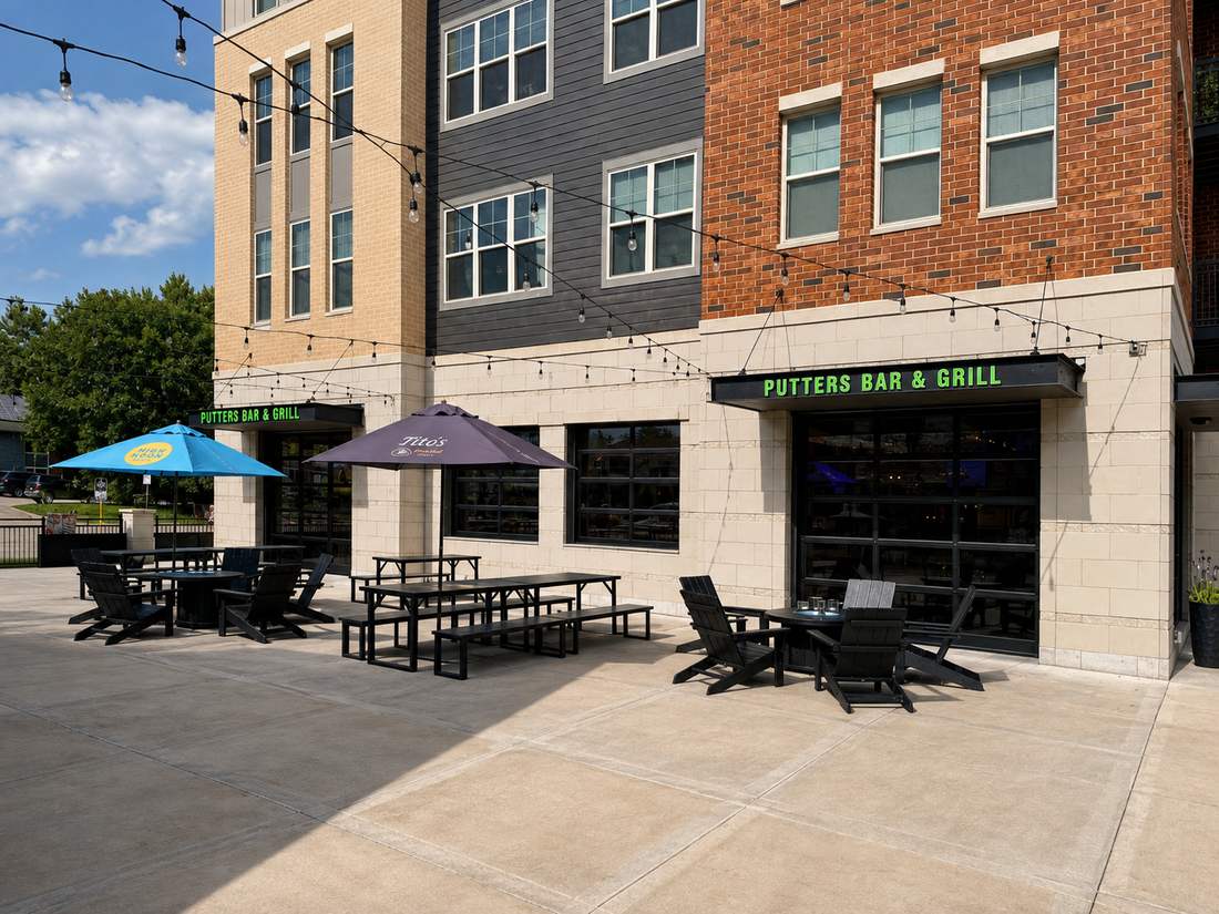 Putters Bar & Grill patio with umbrellas, picnic tables, and string lights under the green sign