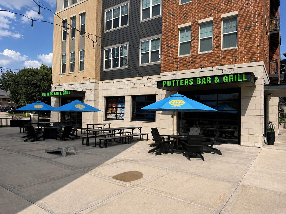 Patio seating with blue umbrellas and Adirondack chairs outside Putters Bar & Grill